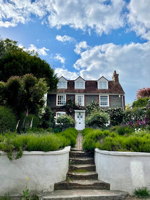 A well-maintained garden featuring a lush, evenly cut green lawn on the right side, bordered by a low wooden fence and a variety of mature trees and dense shrubs on the left side, creating a natural b